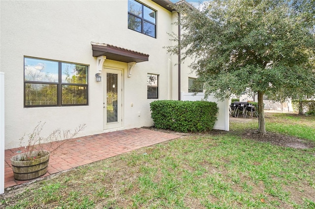 view of exterior entry featuring a patio and a lawn