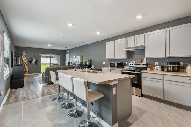 kitchen featuring a breakfast bar, a center island with sink, sink, stainless steel electric range oven, and light hardwood / wood-style floors