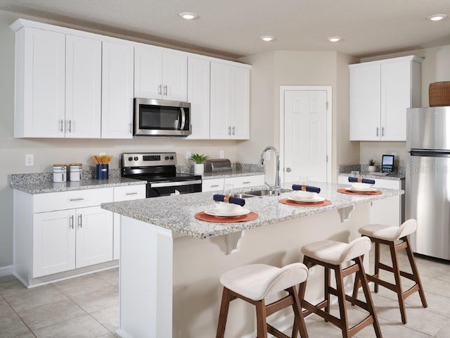 kitchen featuring white cabinets, appliances with stainless steel finishes, a center island with sink, and light stone counters