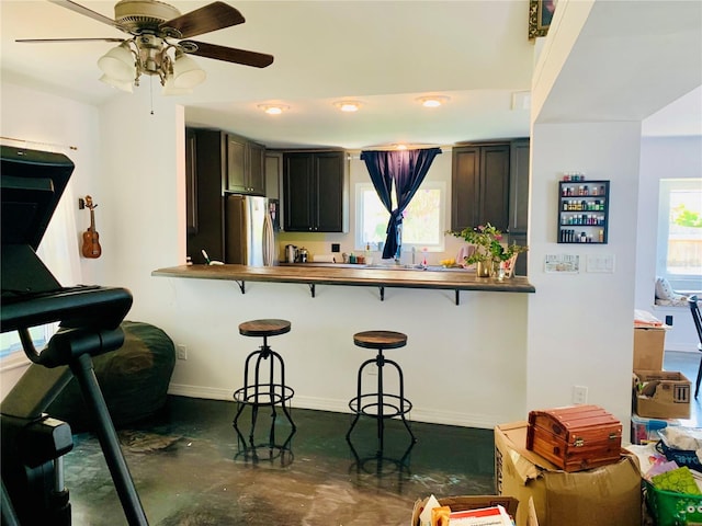 kitchen with a kitchen bar, kitchen peninsula, stainless steel refrigerator, and a healthy amount of sunlight