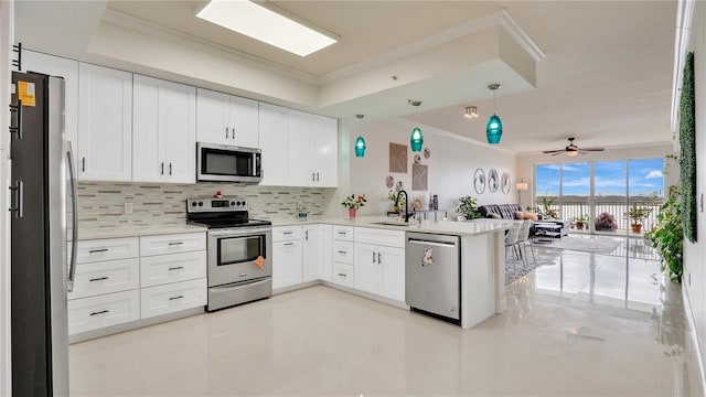 kitchen with stainless steel appliances, light countertops, white cabinets, a sink, and a peninsula