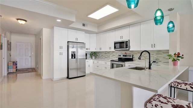 kitchen featuring a peninsula, hanging light fixtures, stainless steel appliances, white cabinetry, and a sink