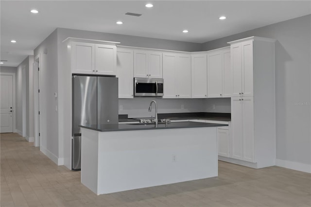 kitchen featuring appliances with stainless steel finishes, light wood-type flooring, sink, a center island with sink, and white cabinets