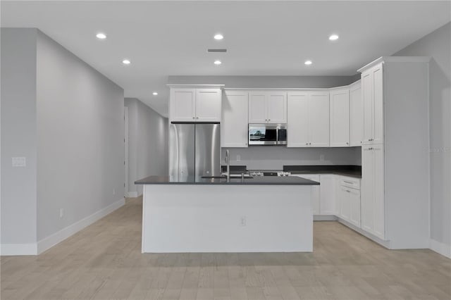 kitchen with appliances with stainless steel finishes, a kitchen island with sink, sink, light hardwood / wood-style flooring, and white cabinetry