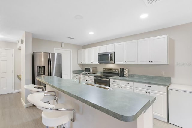 kitchen with a breakfast bar area, white cabinetry, light hardwood / wood-style flooring, and stainless steel appliances