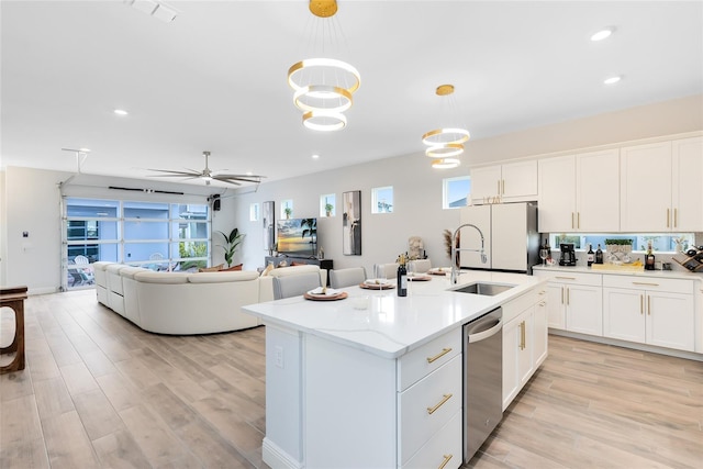 kitchen with stainless steel dishwasher, pendant lighting, a kitchen island with sink, ceiling fan with notable chandelier, and white cabinets