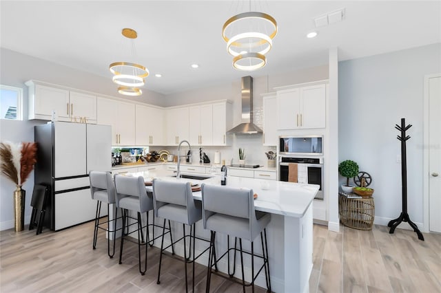 kitchen featuring white cabinets, stainless steel oven, white fridge, wall chimney exhaust hood, and hanging light fixtures