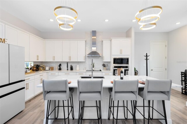 kitchen with wall chimney range hood, oven, backsplash, white cabinets, and white refrigerator