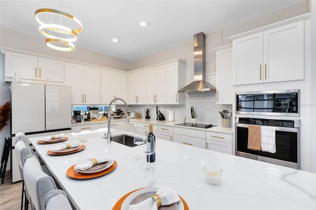 kitchen with pendant lighting, black electric cooktop, wall chimney exhaust hood, sink, and white cabinetry