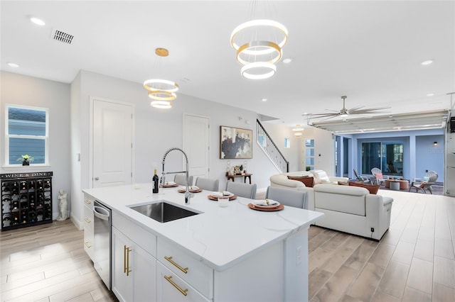 kitchen with sink, hanging light fixtures, white cabinets, and a center island with sink