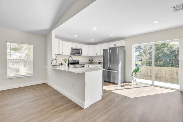 kitchen with light stone counters, light hardwood / wood-style flooring, appliances with stainless steel finishes, kitchen peninsula, and white cabinets