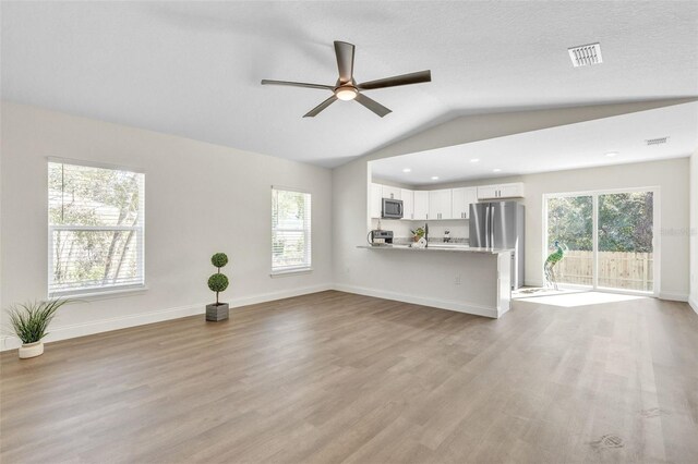 unfurnished living room with vaulted ceiling, plenty of natural light, and light wood-type flooring