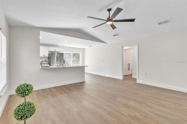 unfurnished living room with ceiling fan, lofted ceiling, a textured ceiling, and light hardwood / wood-style floors