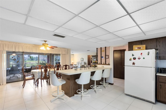 kitchen with a kitchen bar, a paneled ceiling, ceiling fan, and white refrigerator