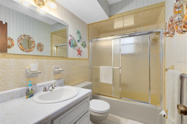 full bathroom with combined bath / shower with glass door, vanity, toilet, and tile walls