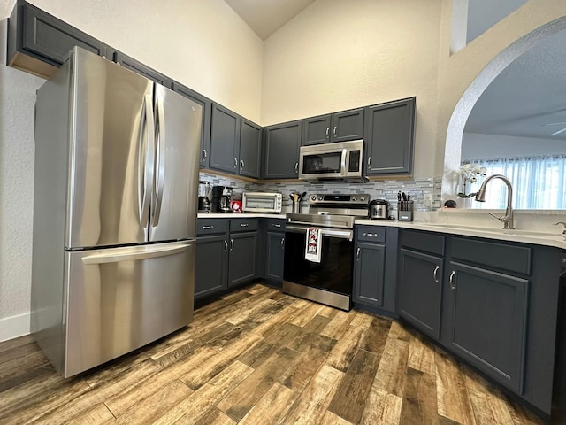 kitchen with sink, stainless steel appliances, vaulted ceiling, and wood-type flooring