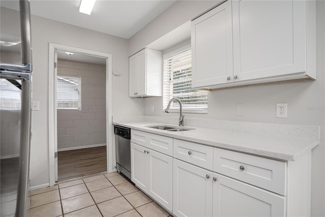 kitchen with stainless steel dishwasher, white cabinetry, sink, light stone counters, and light tile patterned floors