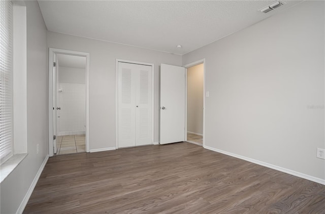 unfurnished bedroom featuring ensuite bathroom, dark hardwood / wood-style floors, and a textured ceiling