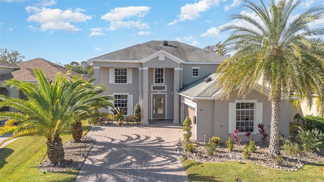 view of front facade with a shingled roof, decorative driveway, a garage, and stucco siding