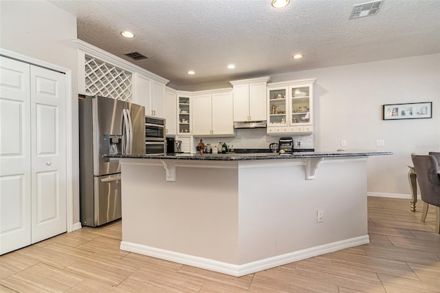 kitchen featuring dark stone countertops, an island with sink, appliances with stainless steel finishes, white cabinetry, and a breakfast bar area