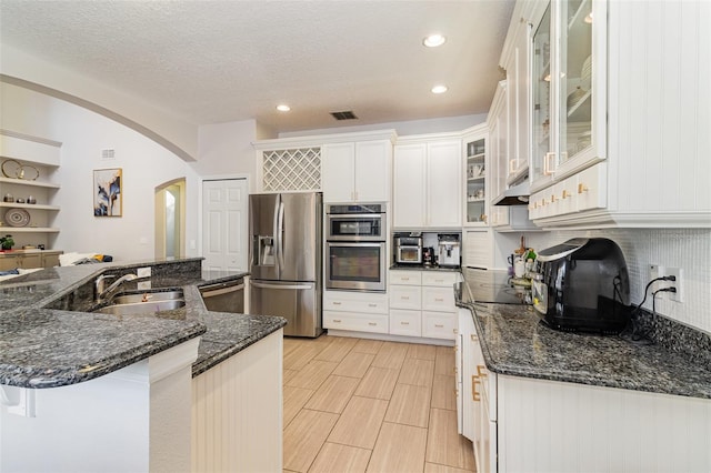 kitchen featuring white cabinets, sink, dark stone countertops, appliances with stainless steel finishes, and a breakfast bar area