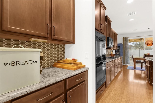 kitchen with light stone countertops, decorative light fixtures, decorative backsplash, black appliances, and light wood-type flooring