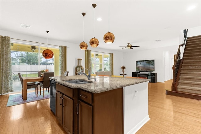 kitchen featuring light stone countertops, a kitchen island with sink, ceiling fan, sink, and pendant lighting