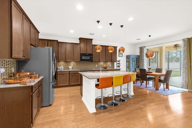 kitchen featuring hanging light fixtures, decorative backsplash, light stone counters, a kitchen island with sink, and a breakfast bar