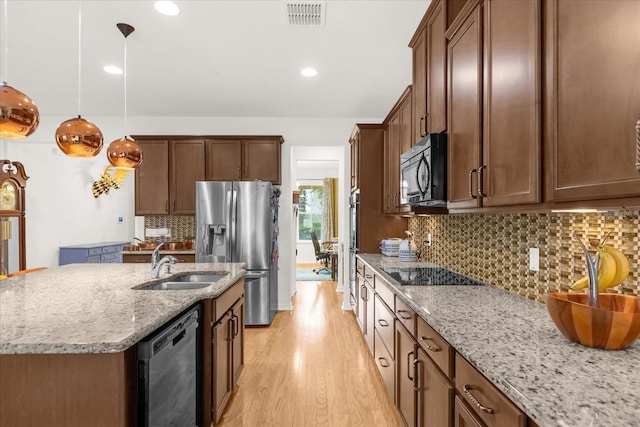 kitchen featuring light stone countertops, sink, black appliances, a center island with sink, and hanging light fixtures