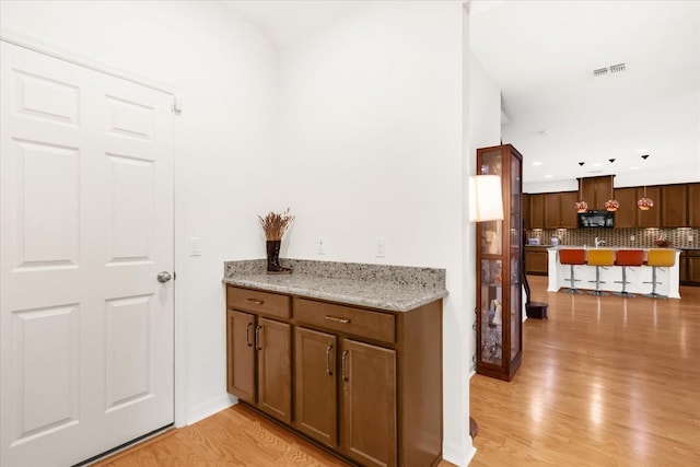 bar with backsplash, light stone countertops, and light wood-type flooring