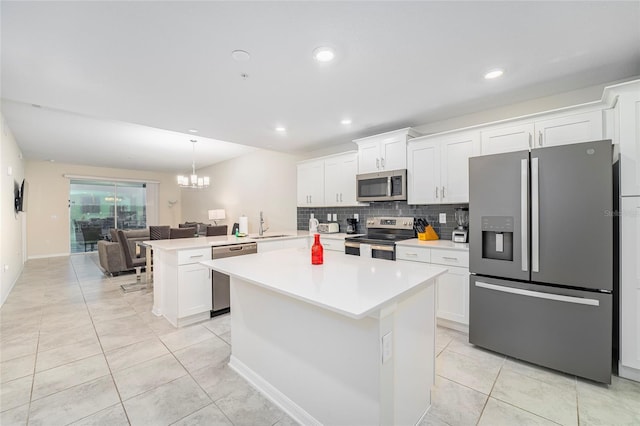 kitchen featuring stainless steel appliances, an inviting chandelier, kitchen peninsula, pendant lighting, and white cabinets