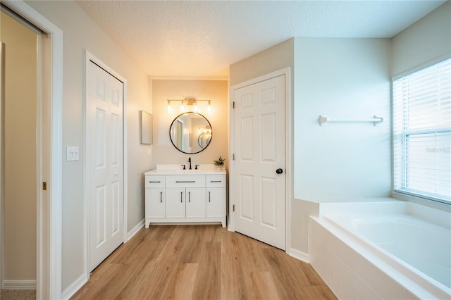 bathroom with vanity, a relaxing tiled tub, a textured ceiling, and hardwood / wood-style flooring