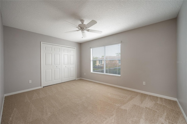 unfurnished bedroom featuring ceiling fan, light colored carpet, a textured ceiling, and a closet