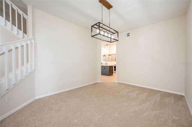 carpeted spare room featuring a textured ceiling and an inviting chandelier