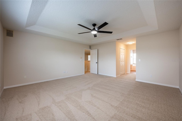 empty room with ceiling fan, a textured ceiling, light carpet, and a tray ceiling