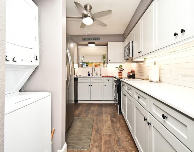 kitchen featuring stainless steel appliances, sink, white cabinets, stacked washer and dryer, and dark hardwood / wood-style floors