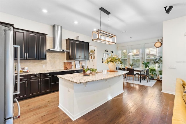 kitchen featuring wall chimney range hood, pendant lighting, a center island, light hardwood / wood-style floors, and a breakfast bar area