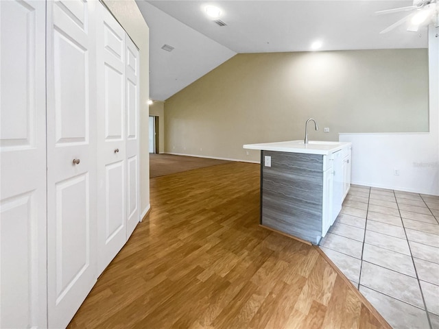 kitchen with vaulted ceiling, ceiling fan, a kitchen island with sink, sink, and light hardwood / wood-style floors