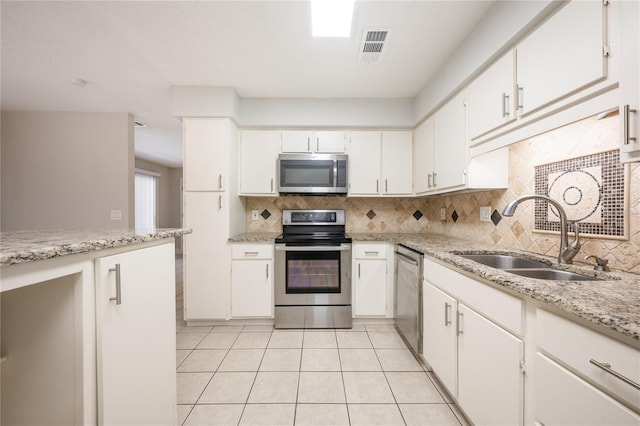 kitchen with appliances with stainless steel finishes, tasteful backsplash, sink, light tile patterned floors, and white cabinetry