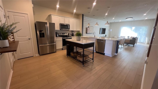 kitchen with stainless steel appliances, sink, pendant lighting, light hardwood / wood-style flooring, and white cabinetry