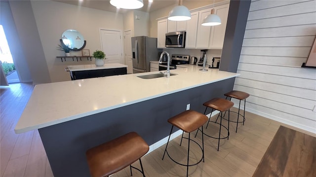 kitchen with stainless steel appliances, kitchen peninsula, light hardwood / wood-style floors, decorative light fixtures, and a breakfast bar