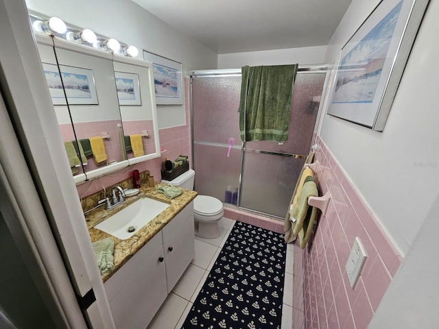 bathroom with tile patterned floors, vanity, a shower with door, tile walls, and toilet