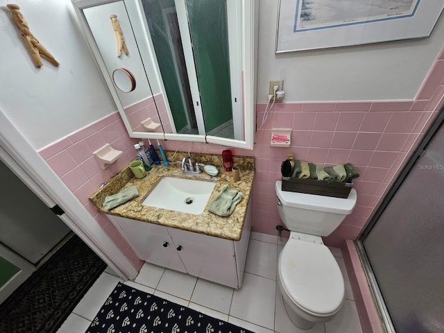 bathroom featuring tile patterned floors, vanity, a shower with door, tile walls, and toilet