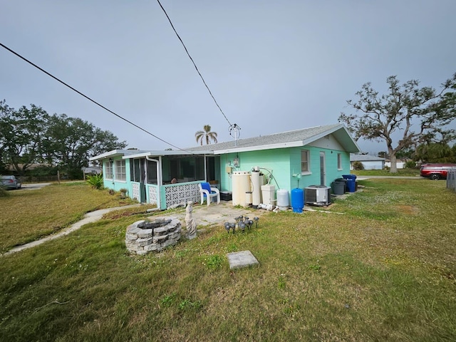 rear view of property featuring a lawn, a sunroom, cooling unit, and an outdoor fire pit