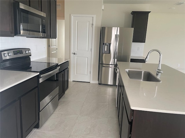 kitchen with decorative backsplash, sink, appliances with stainless steel finishes, an island with sink, and light tile patterned floors