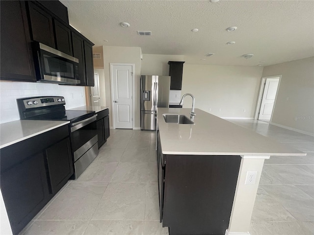 kitchen with an island with sink, stainless steel appliances, light tile patterned flooring, a textured ceiling, and sink