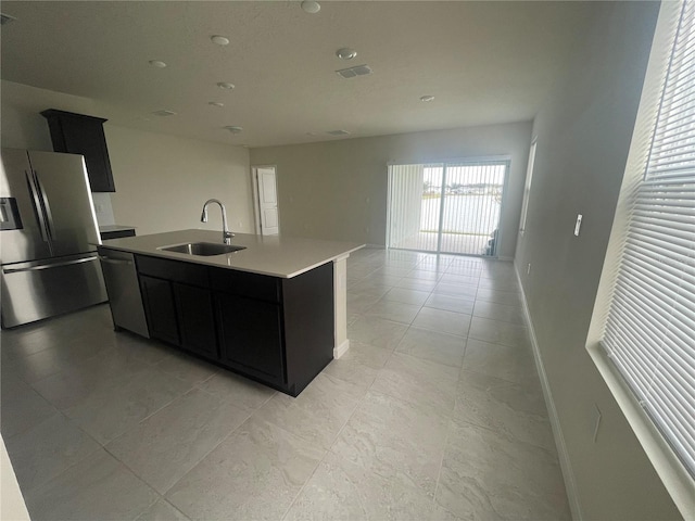 kitchen with light tile patterned floors, appliances with stainless steel finishes, an island with sink, and sink