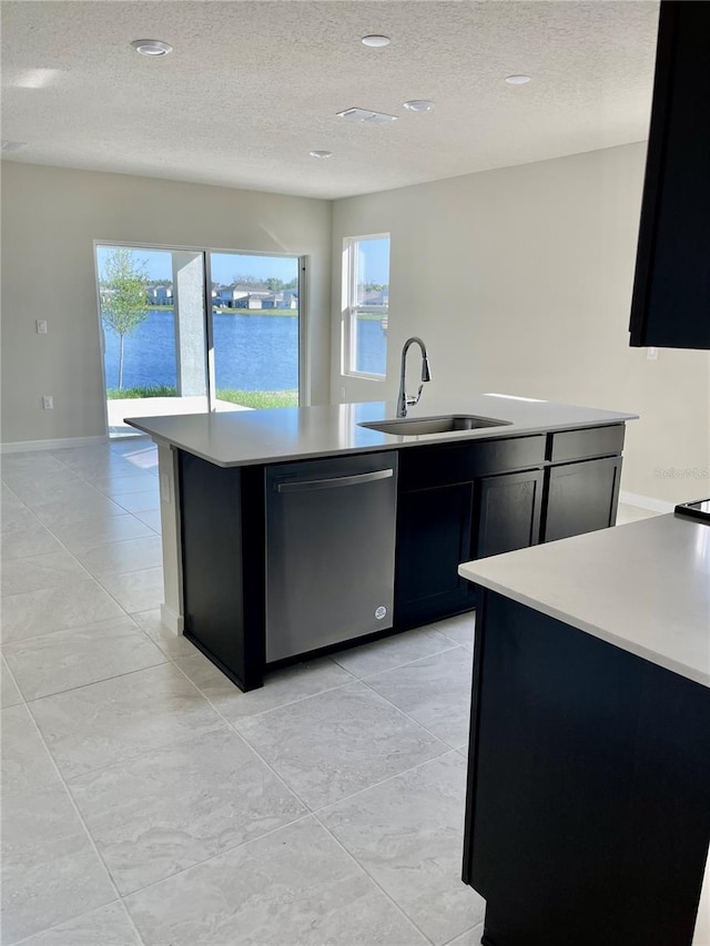 kitchen featuring light tile patterned floors, a center island with sink, stainless steel dishwasher, a water view, and sink