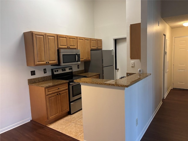 kitchen with kitchen peninsula, light hardwood / wood-style floors, dark stone counters, and appliances with stainless steel finishes