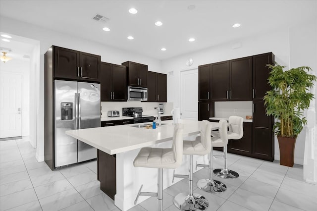 kitchen with a kitchen breakfast bar, dark brown cabinets, stainless steel appliances, sink, and a center island with sink